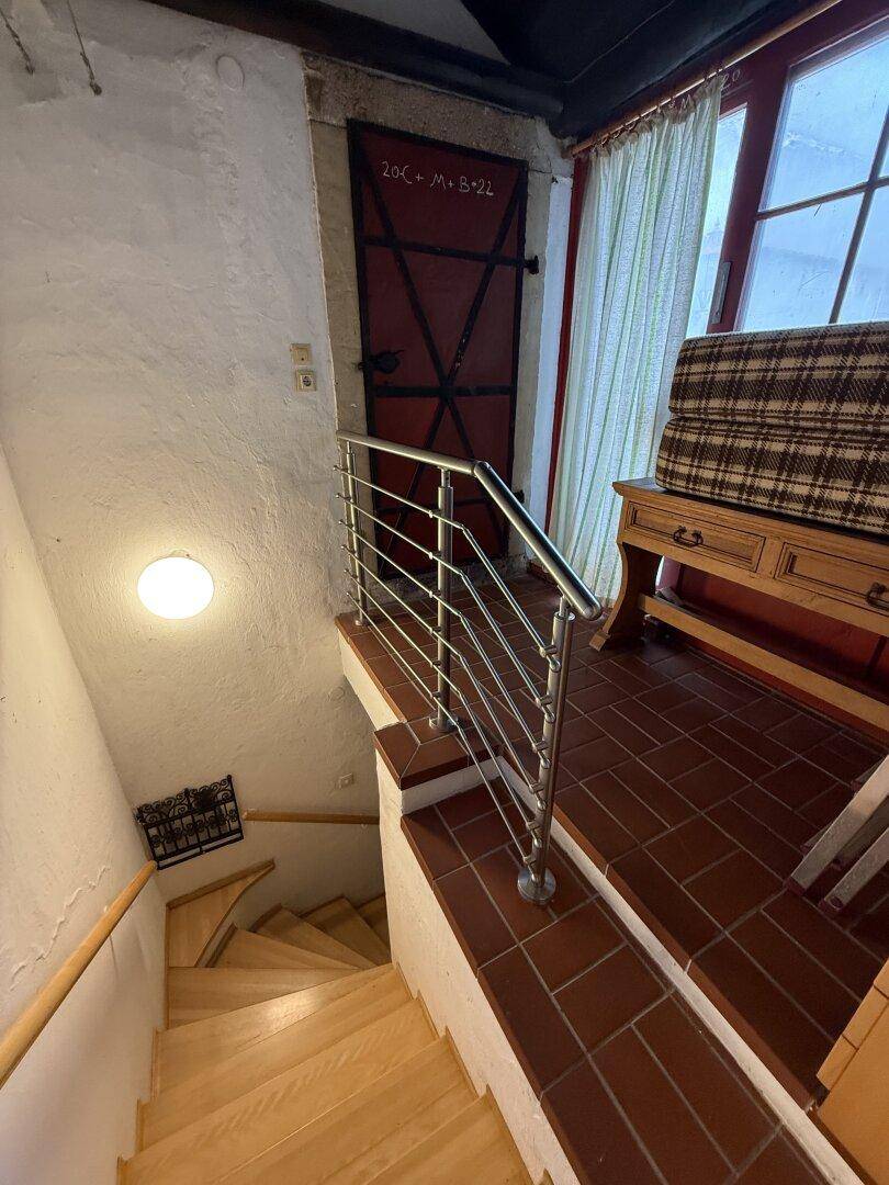 Treppenhaus mit Holzstufen, Fliesenboden und modernem Edelstahlgeländer.