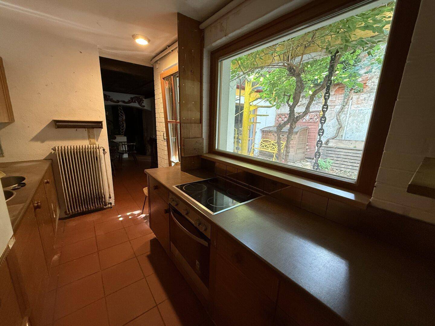 Küche mit Kochfeld, Backofen und großem Fenster mit Blick auf den Innenhof.