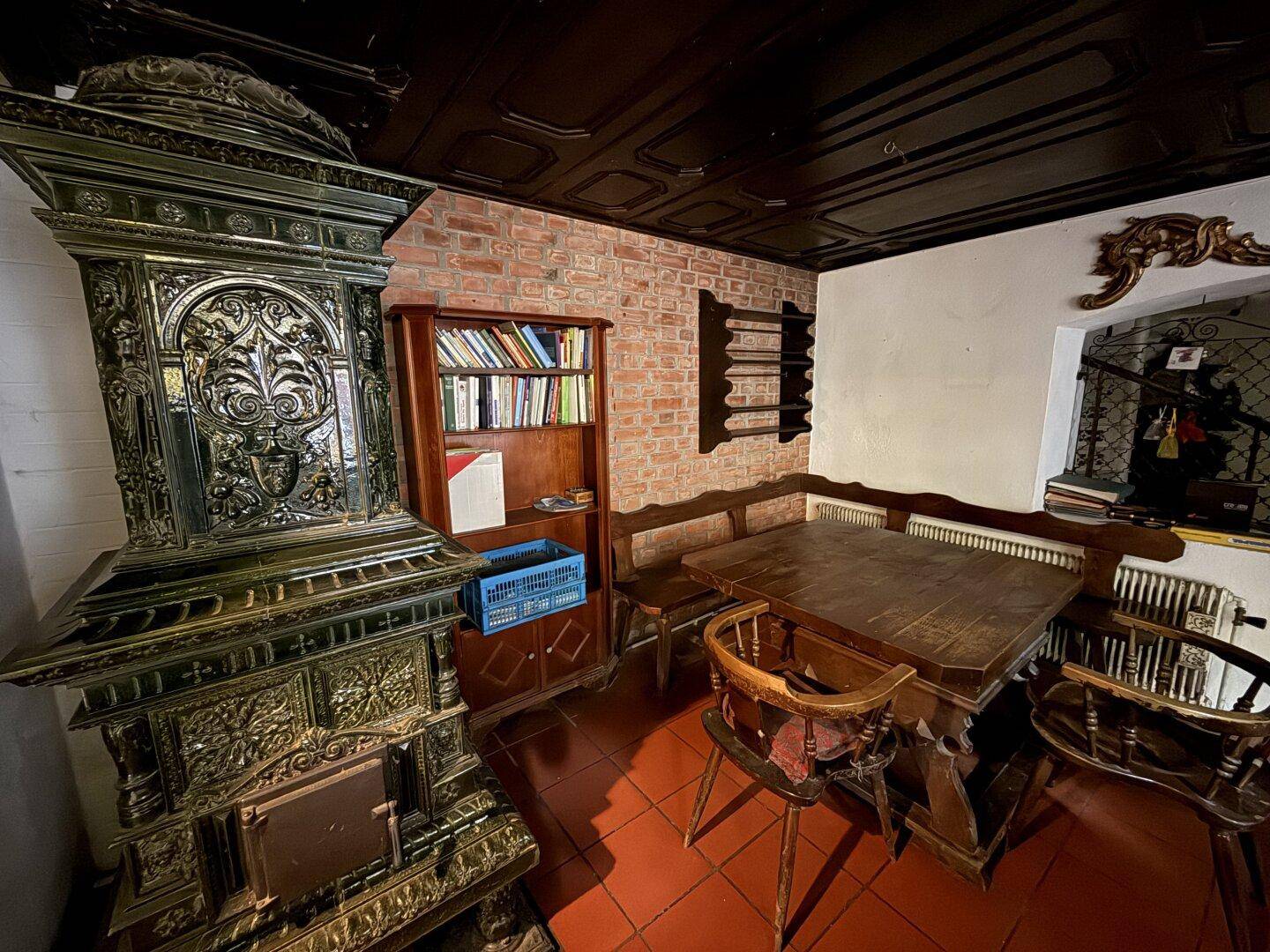Rustikaler Essbereich mit Kachelofen, Holztisch und traditioneller Holzdecke.