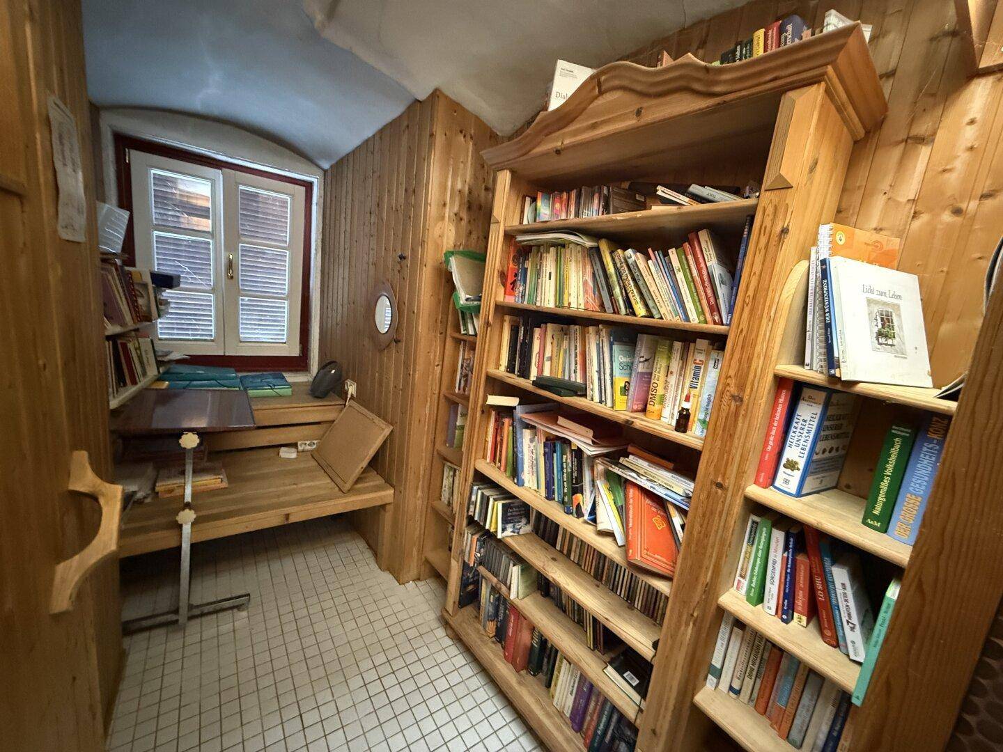 Kleines Arbeitszimmer mit Holzvertäfelung, Bücherregalen und einem Fenster.
