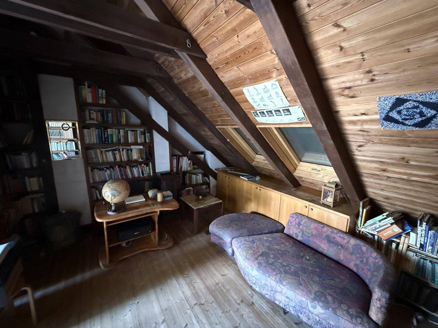 Gemütliches Dachzimmer mit Holzwänden, Bücherregalen, Liegefläche und Dachfenster.