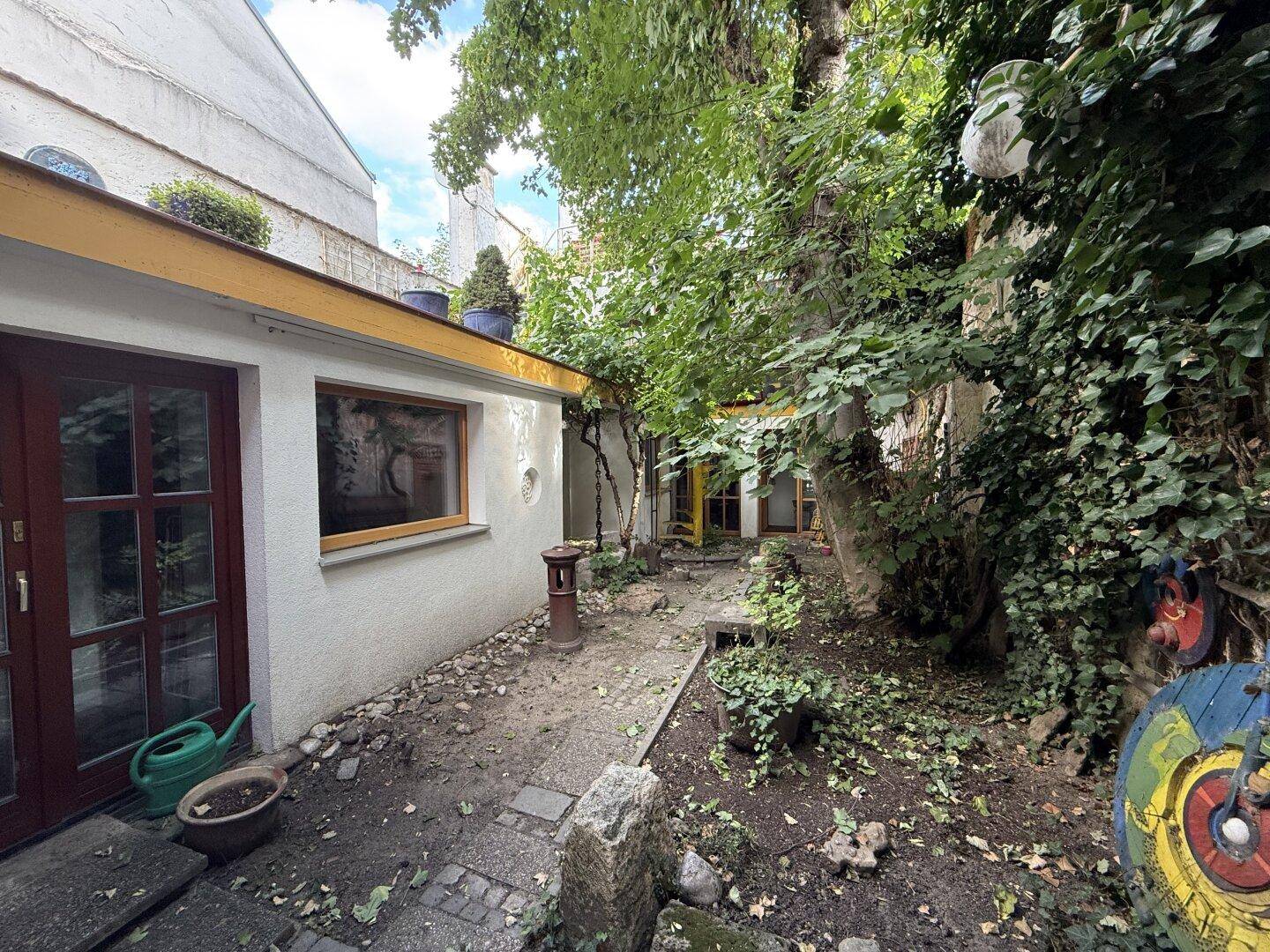Verwinkelter Gartenbereich mit viel Grün, Bäumen und einem gepflasterten Weg.