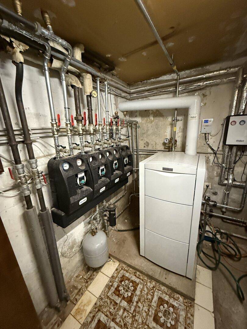 Heizungsraum im Keller mit moderner Heizungsanlage und zahlreichen Rohrleitungen.