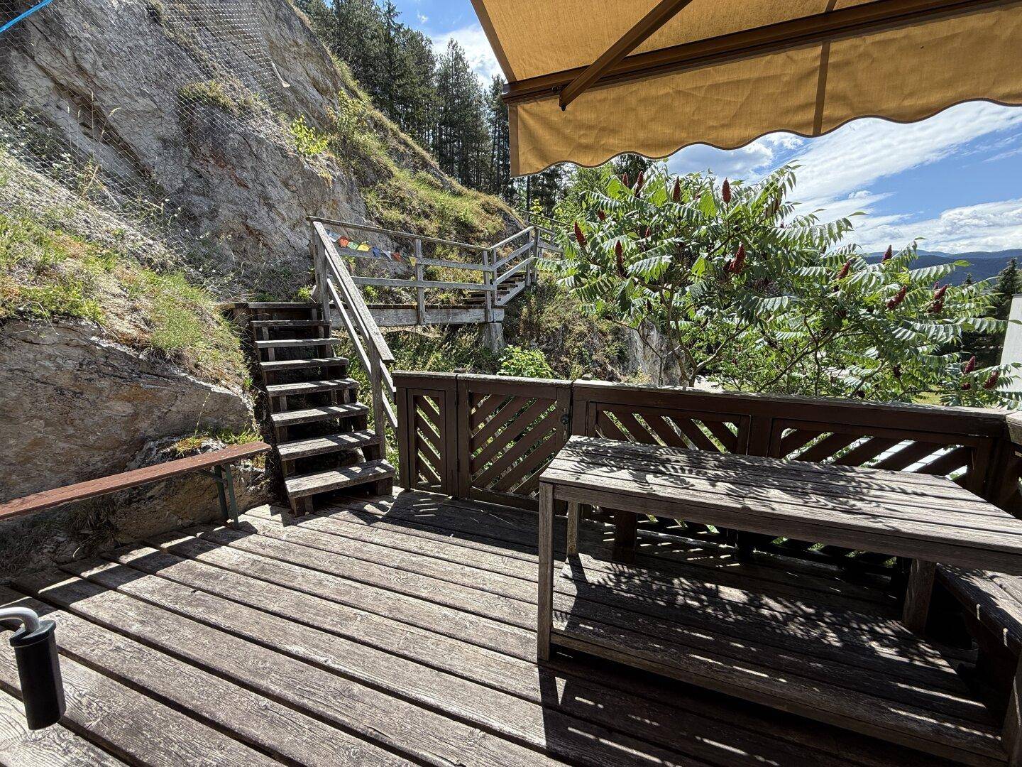 Geräumige Holzterrasse mit Esstisch und Markise, bietet einen weiten Blick in die Landschaft.