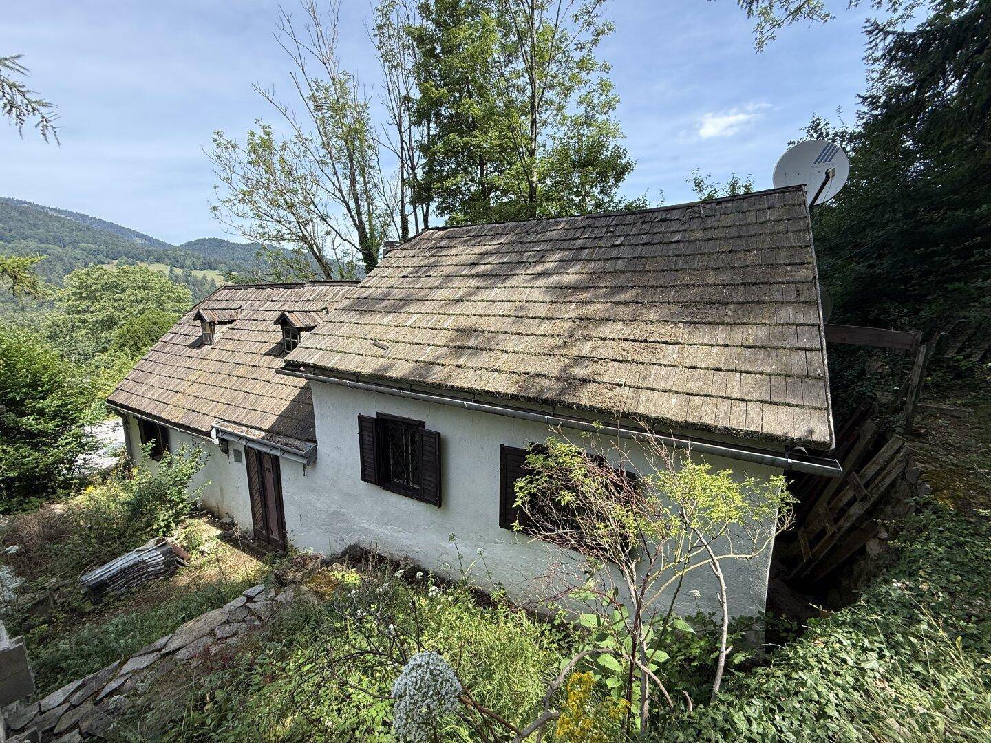 Rückansicht eines Gebäudeteils mit traditionellem Holzdach und weißer Fassade, umgeben von Natur.