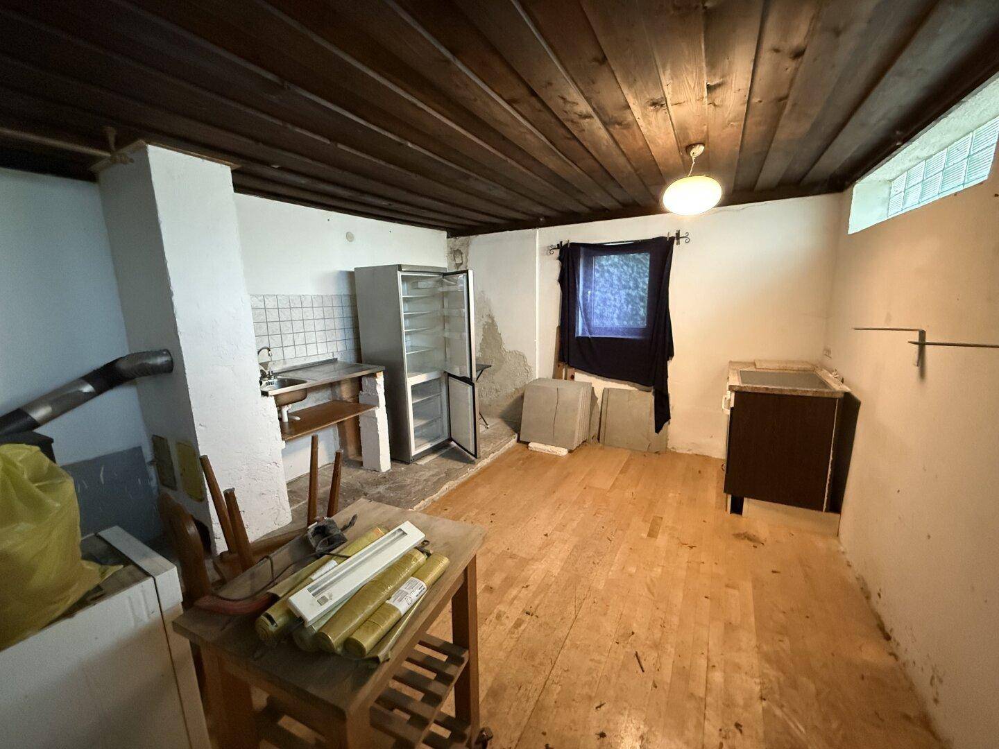 Einfache Küchenzeile mit Holzdecke, Dielenboden und einem Kühlschrank, renovierungsbedürftig.
