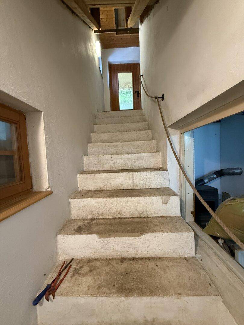 Schmale Steintreppe mit Seilgeländer führt in die obere Etage, mit Holztür am Ende.