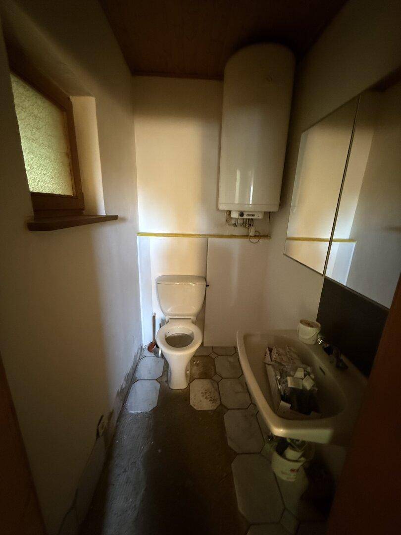 Kleines WC mit Toilette, Waschbecken und Boiler, gefliestem Boden und Fenster.