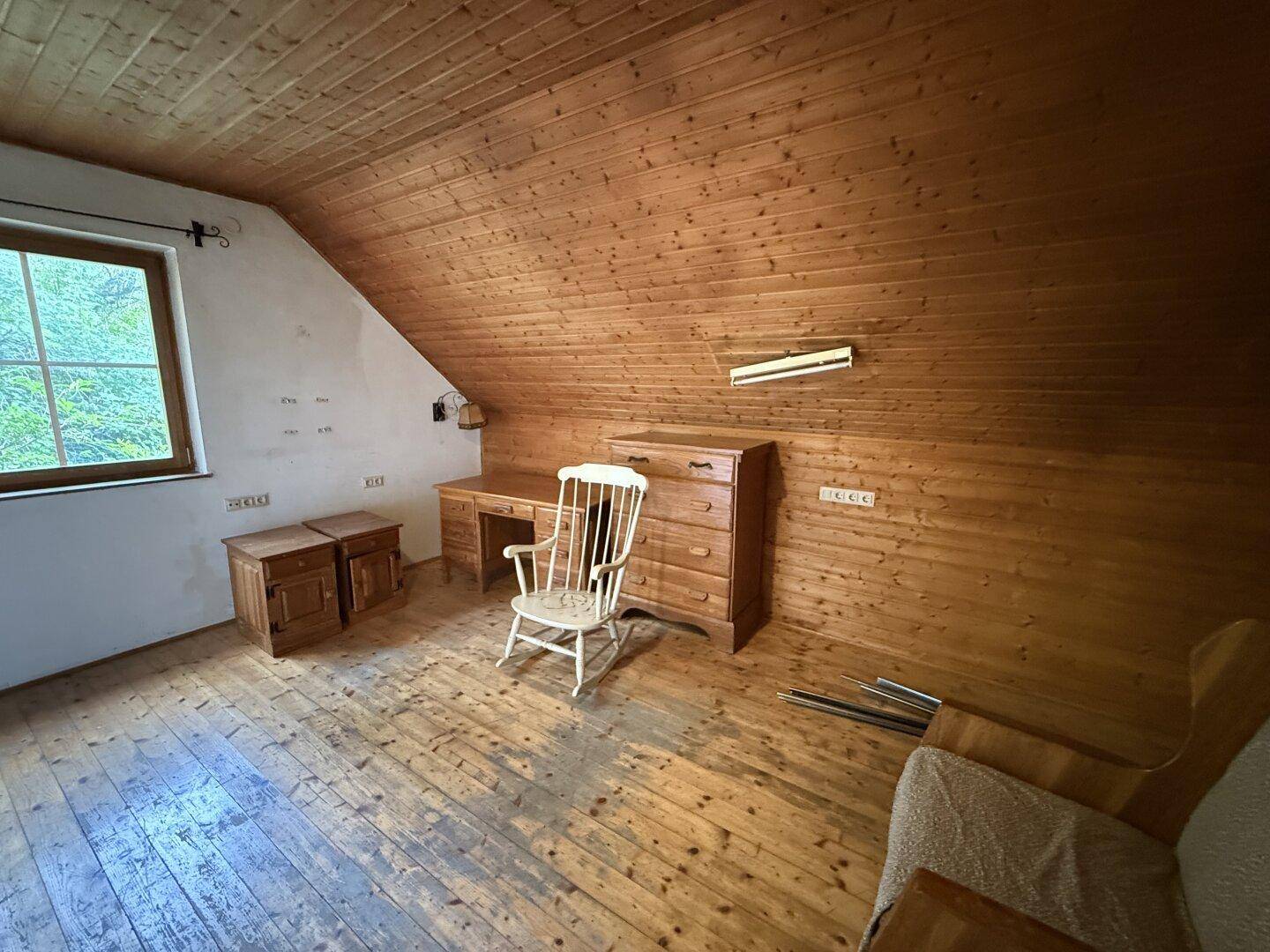 Gemütliches Zimmer im Dachgeschoss mit Holzverkleidung, Dielenboden und einfacher Möblierung.