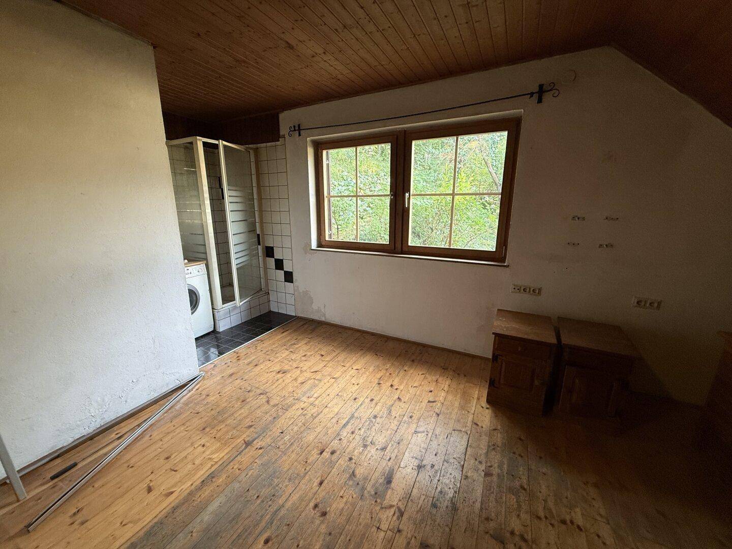 Dachgeschosszimmer mit Holzverkleidung, Dielenboden und integrierter Duschkabine und Waschmaschine.