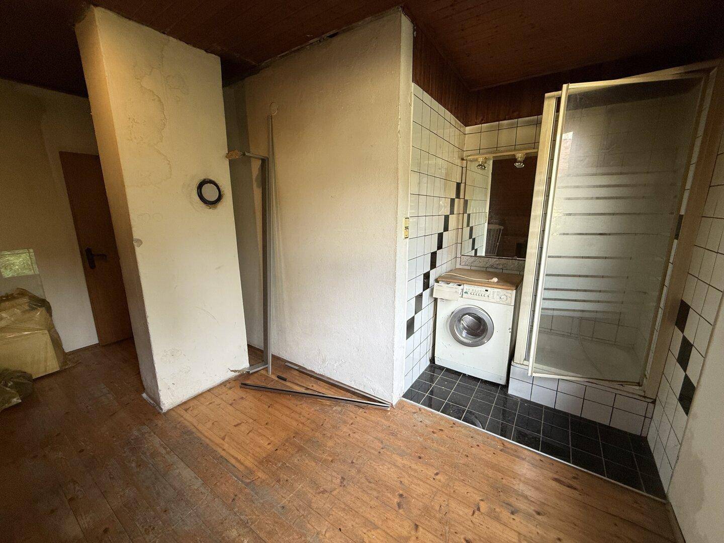 Integrierter Duschbereich mit Waschmaschine in einem Dachgeschosszimmer mit Holzboden.