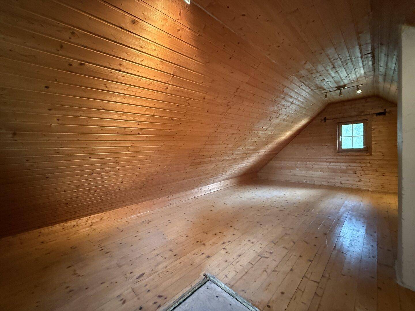 Leerer Dachbodenraum mit vollständiger Holzverkleidung und Dielenboden, bereit zum Ausbau.