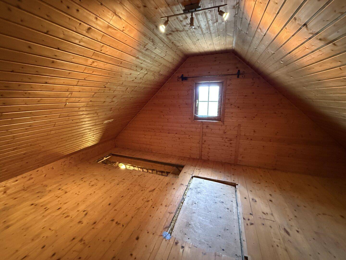 Geräumiger Dachboden mit Holzverkleidung und kleinem Fenster, bietet viel Potenzial.