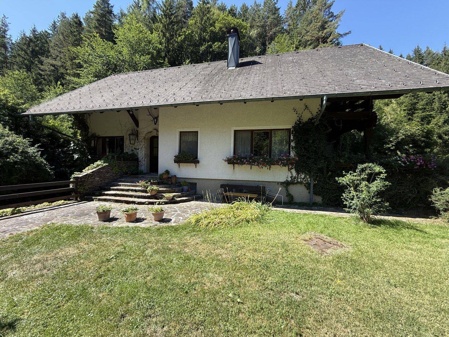 Charmantes Landhaus mit weißer Fassade, umgeben von einem gepflegten Rasen und Wald.