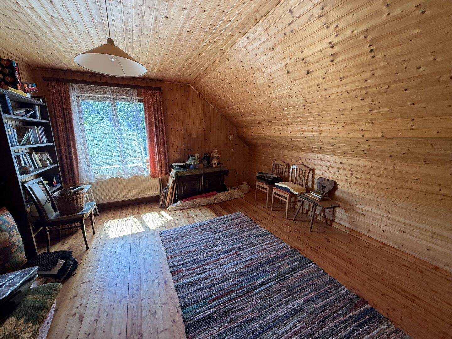 Gemütlicher Wohnbereich im Dachgeschoss mit Holzvertäfelung, Teppich und natürlichem Lichteinfall.