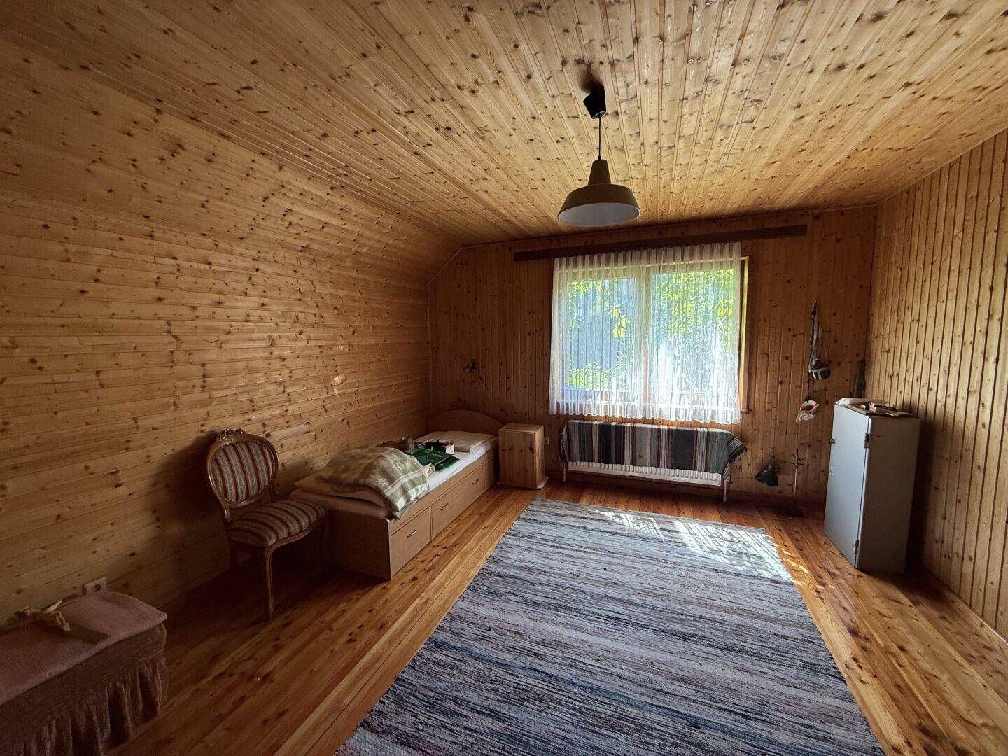 Helles Schlafzimmer im Dachgeschoss mit Holzvertäfelung, Einzelbett und Teppichboden.