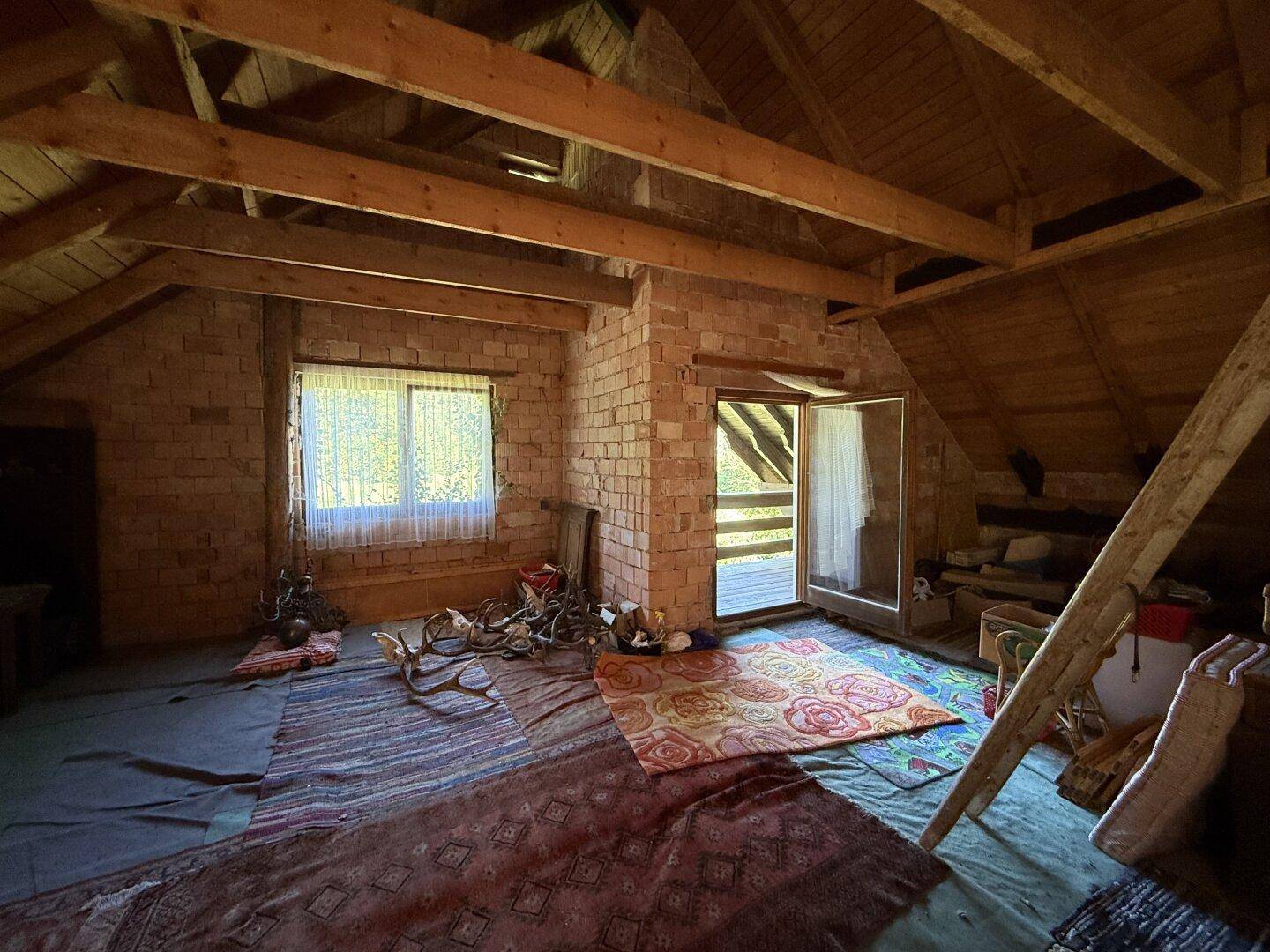 Unausgebauter Dachbodenraum mit sichtbaren Holzbalken und Ziegelwänden, bereit für den Ausbau.