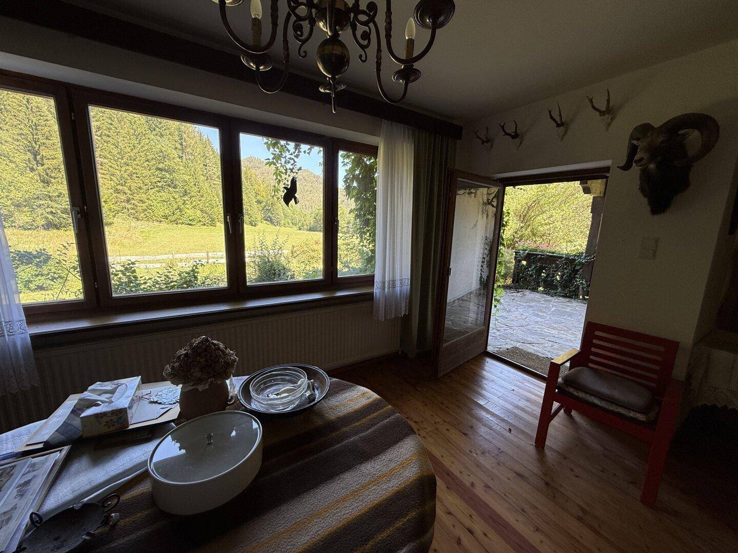 Gemütliches Zimmer mit Holzboden, großen Fenstern und weitem Blick ins Grüne, mit Zugang zur Terrasse.