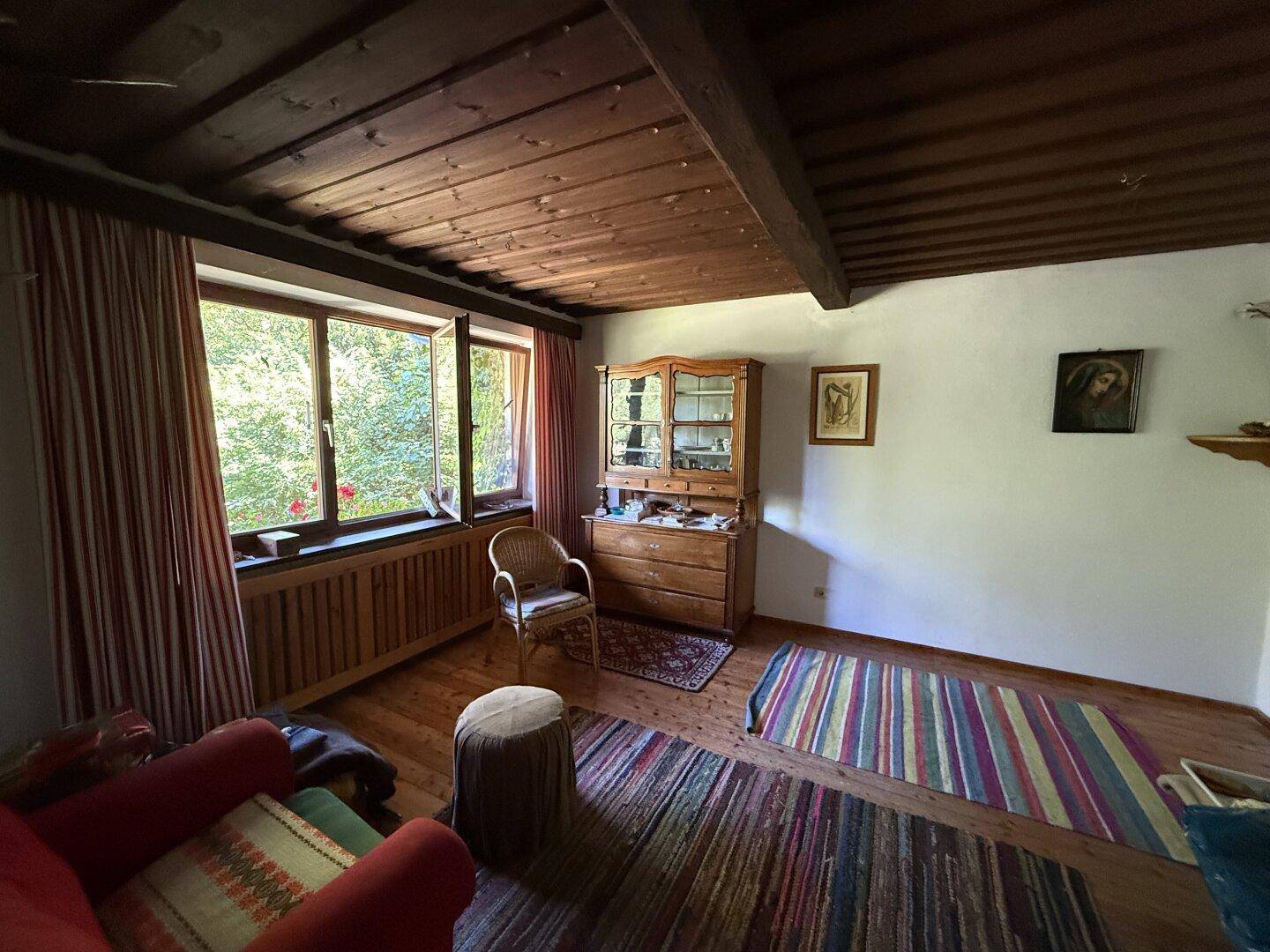 Gemütliches Wohnzimmer mit Holzboden, weiß gestrichenen Wänden und einem schönen Blick ins Grüne.