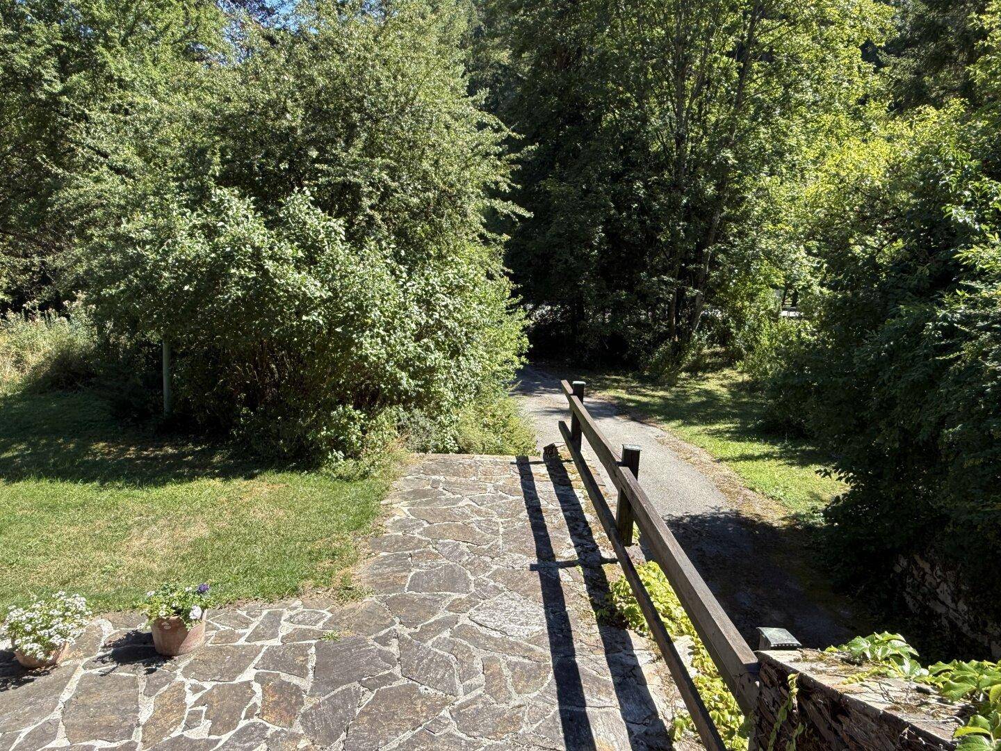 Steinweg führt durch den gepflegten Garten in eine grüne, bewaldete Umgebung mit viel Natur.