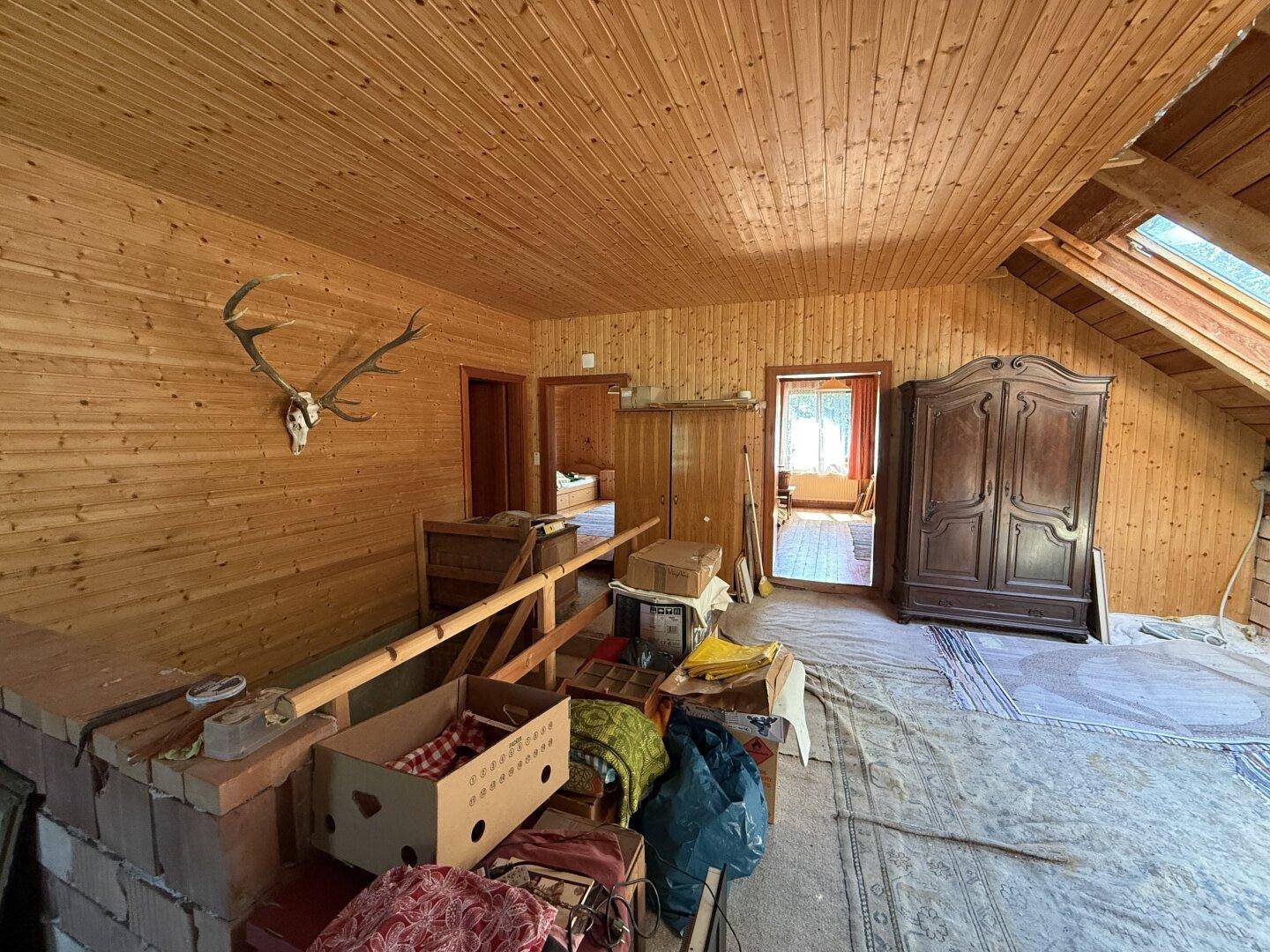 Geräumiger Dachboden mit Holzverkleidung an Wänden und Decke, traditionellen Möbeln und Hirschgeweih.