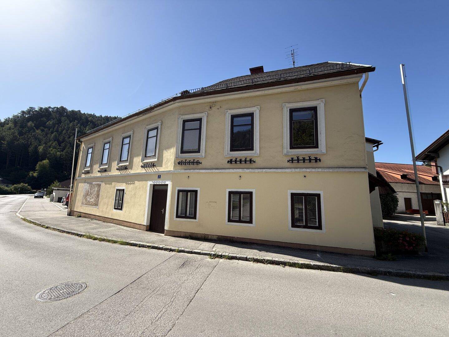 Historisches gelbes Haus mit dunklen Fenstern und Blick auf die umliegende Landschaft.