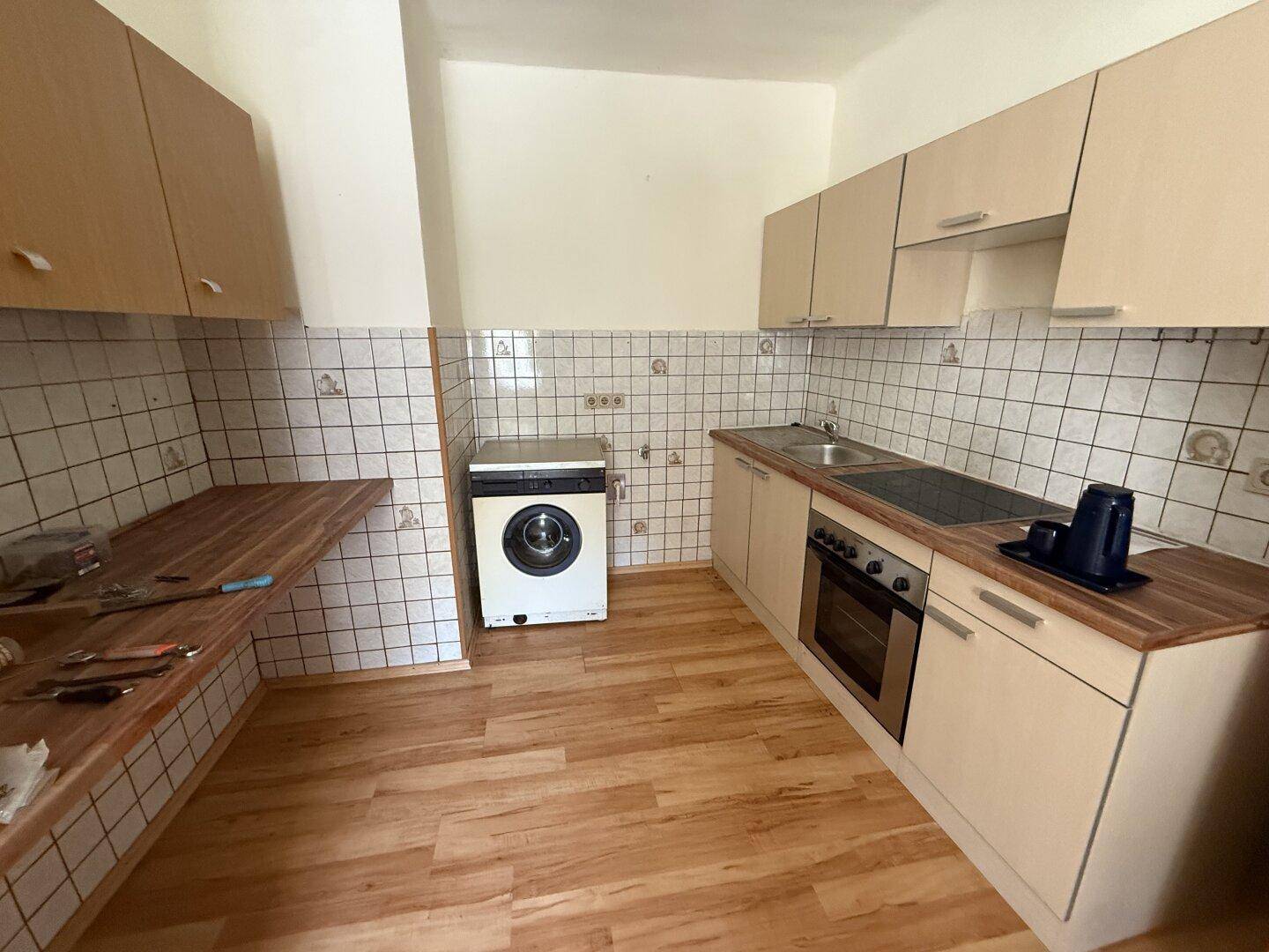Funktionale Küche mit hellen Holzschränken, Fliesenrückwand und integrierten Geräten.