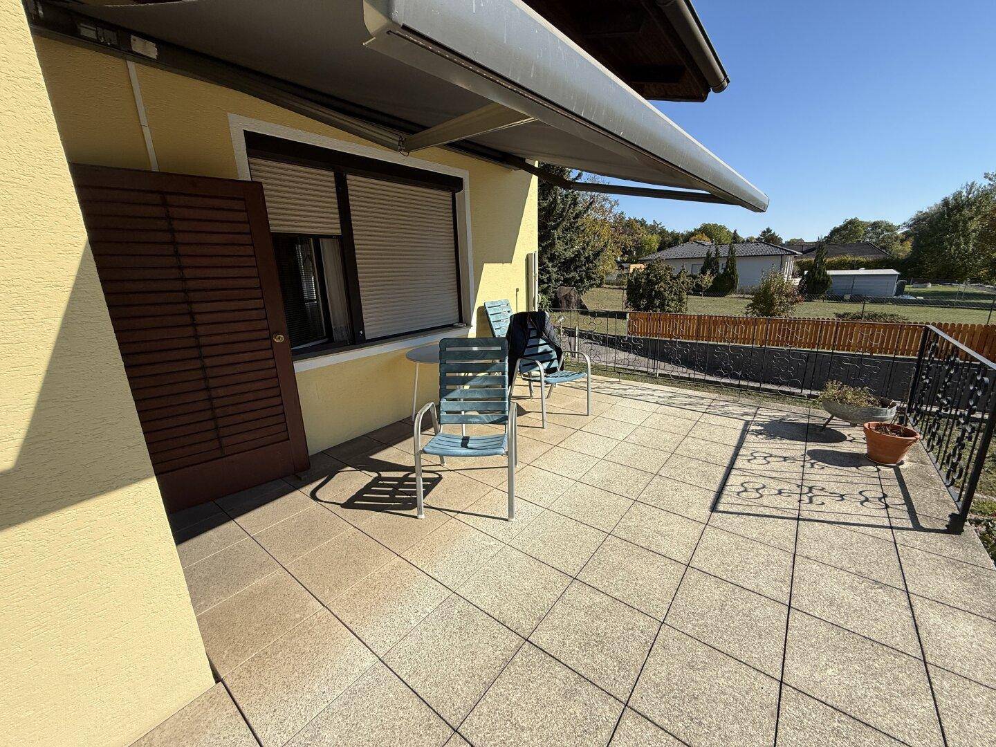 Sonniger Terrassenbereich mit Fliesenboden, Markise und Sitzgelegenheiten im Freien.