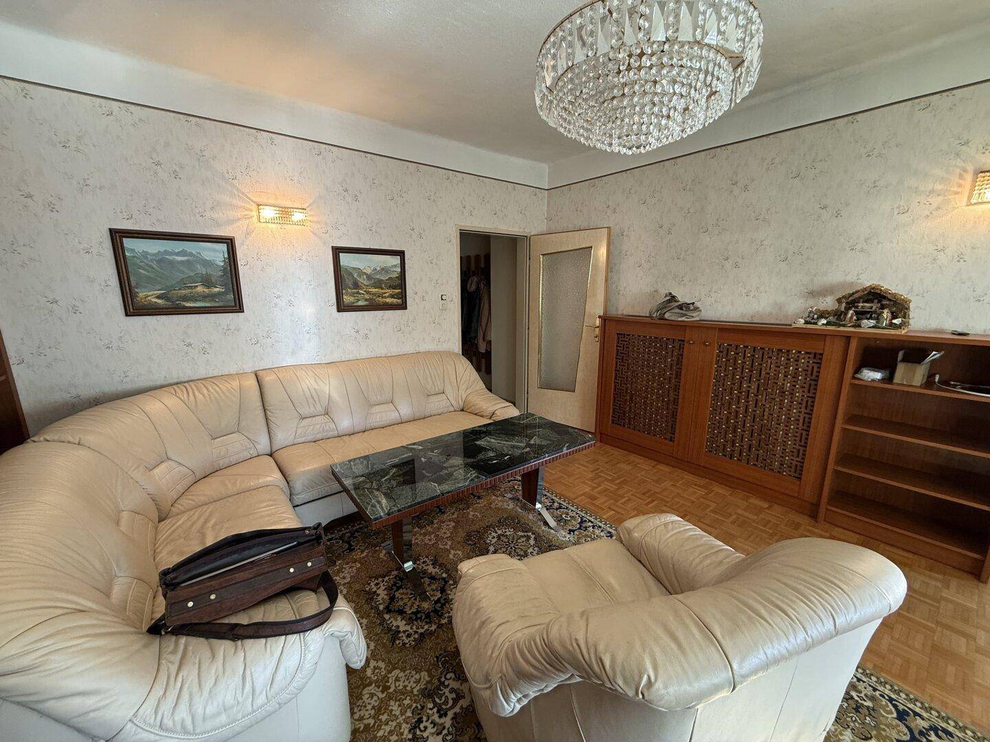 Gemütliches Wohnzimmer mit Ledersofa, Kronleuchter und Parkettboden im klassischen Stil.