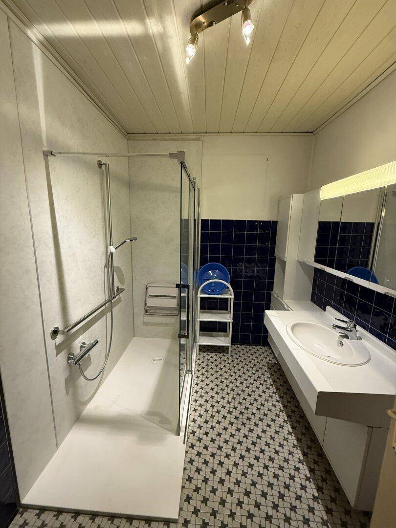 Helles Badezimmer mit barrierefreier Dusche, Waschtisch und blauen Akzentfliesen.