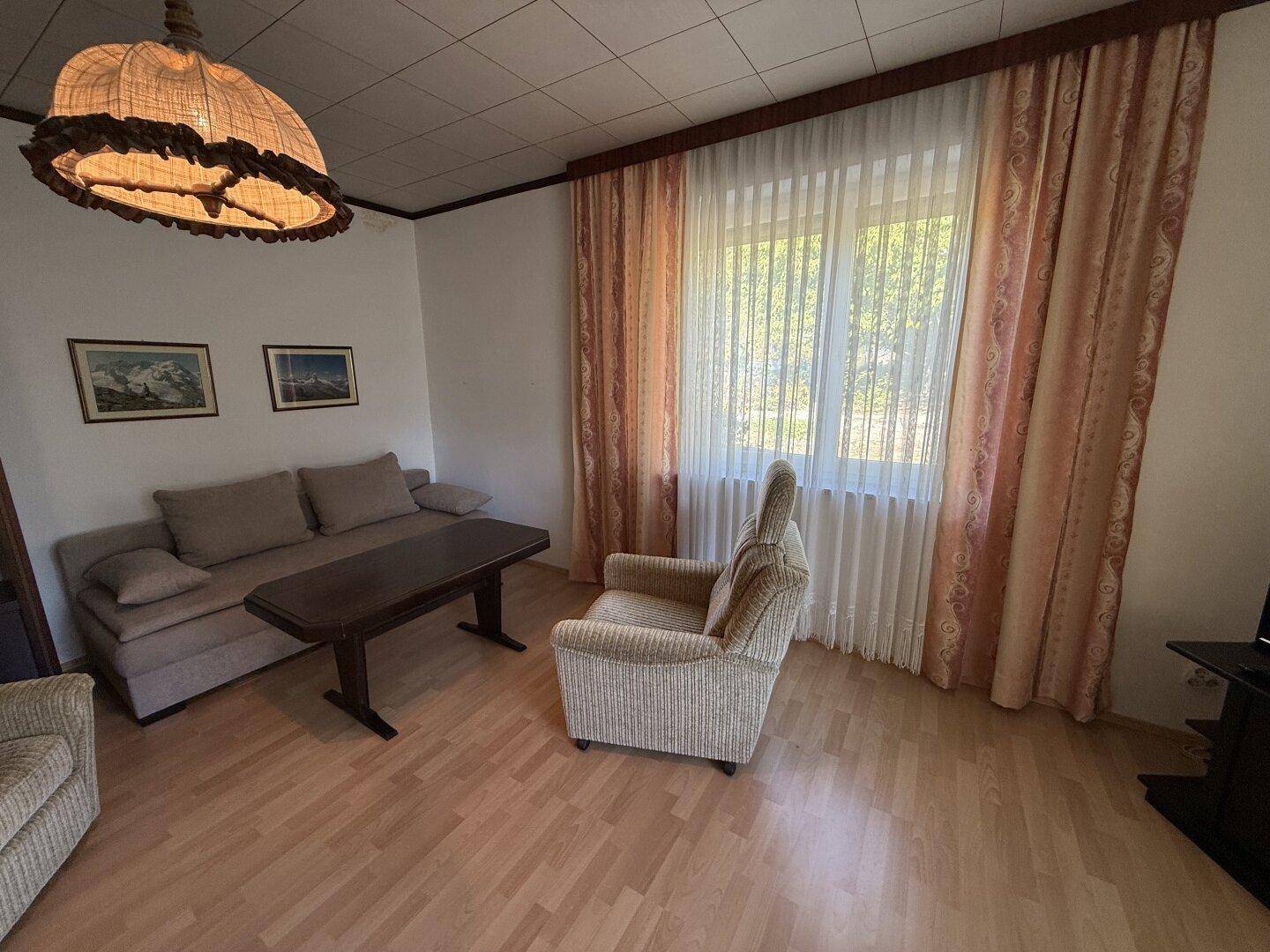 Wohnzimmer mit hellem Laminatboden, bequemen Sesseln und großen Fenstern.