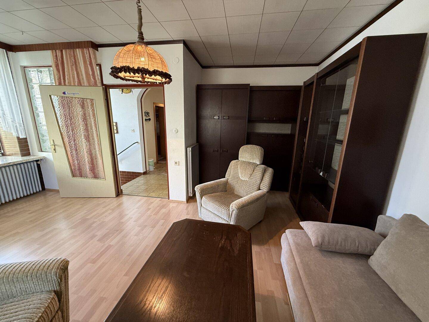 Helles Wohnzimmer mit Laminatboden, Schränken und Blick auf den Eingangsbereich.