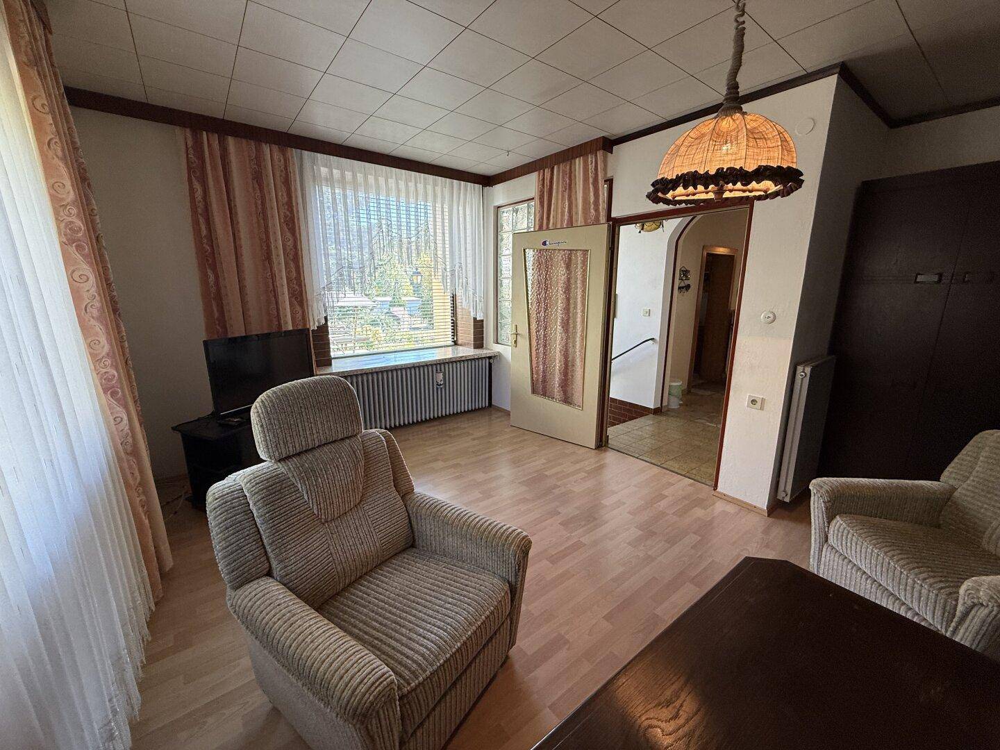 Wohnzimmer mit Laminatboden, bequemen Sitzgelegenheiten und Fenster mit Jalousien.