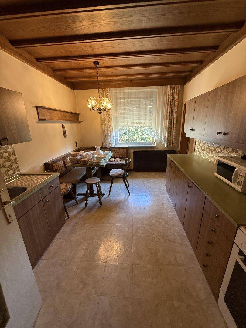 Gemütliche Küche mit Essbereich, Holzmöbeln, gefliestem Boden und sichtbaren Deckenbalken.