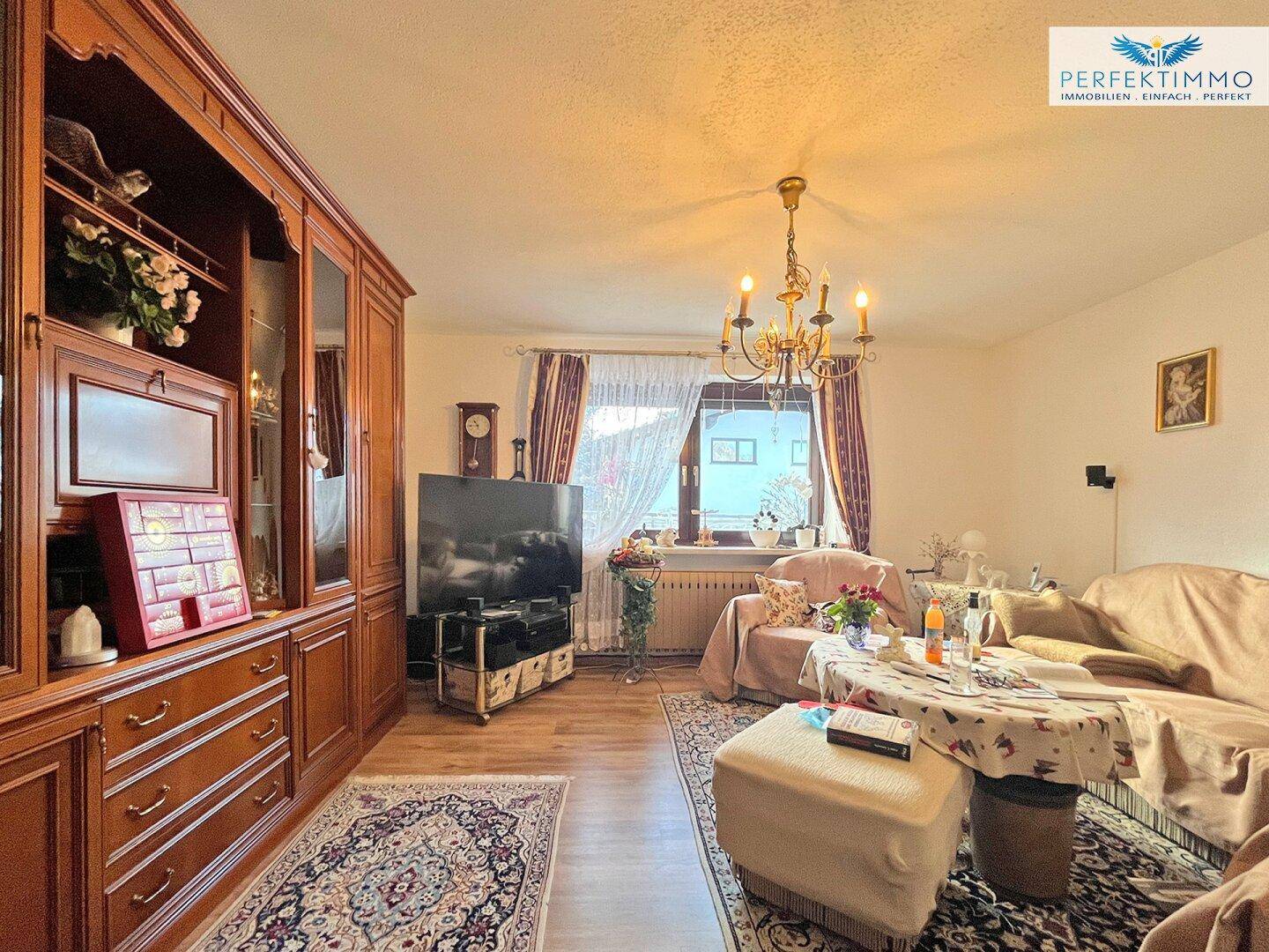 Geräumiges Wohnzimmer mit klassischem Holzschrank, Kronleuchter und Teppichboden.