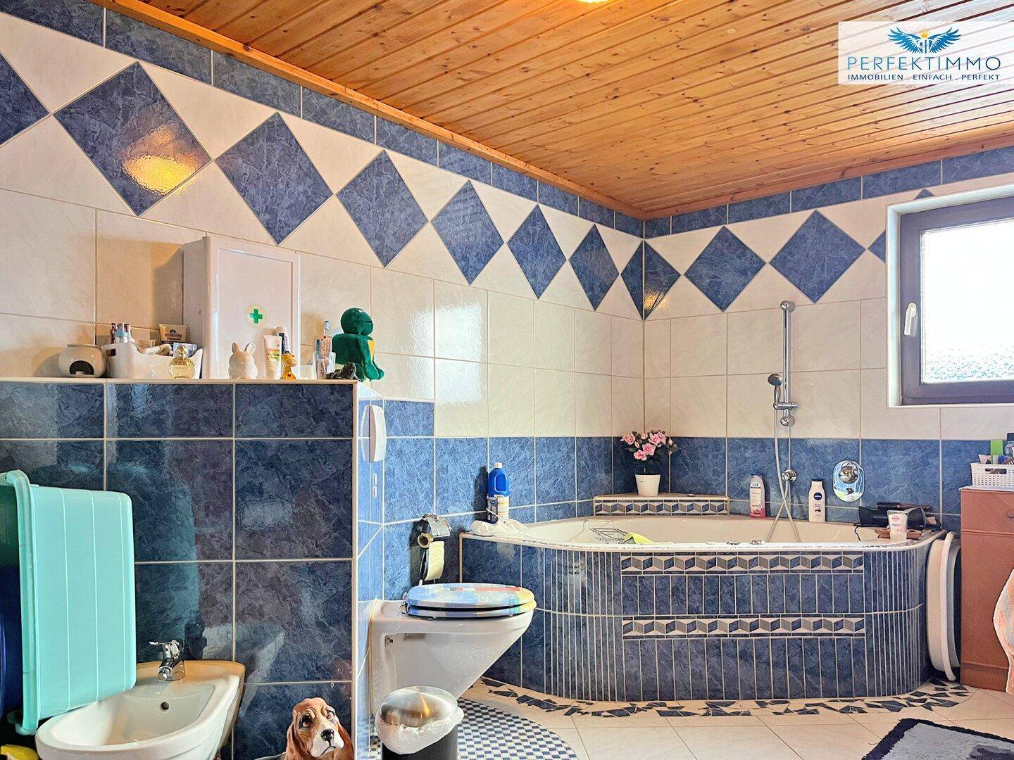 Badezimmer mit blauen und weißen Fliesen, Eckbadewanne und Holzdecke.