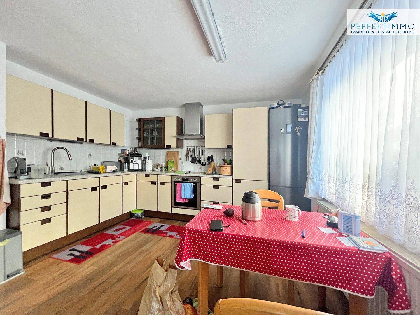Geräumige Wohnküche mit Esstisch, hellen Schränken und großem Fenster.