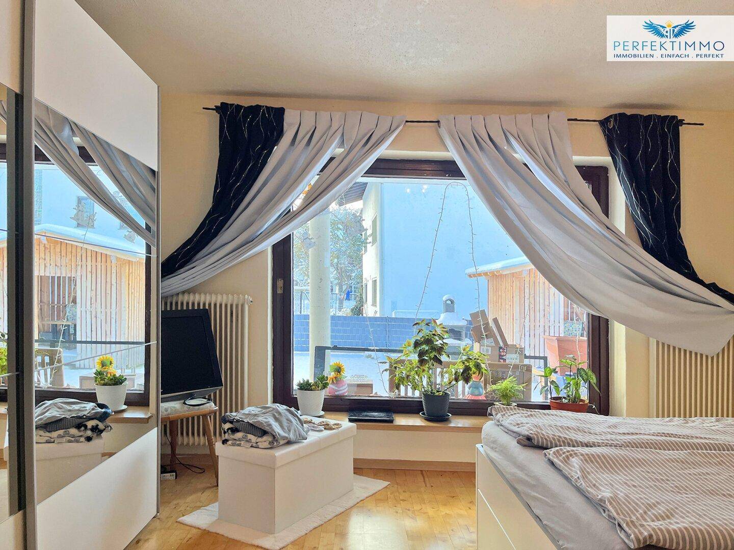 Helles Schlafzimmer mit großem Fenster, Holzboden und Blick ins Grüne.