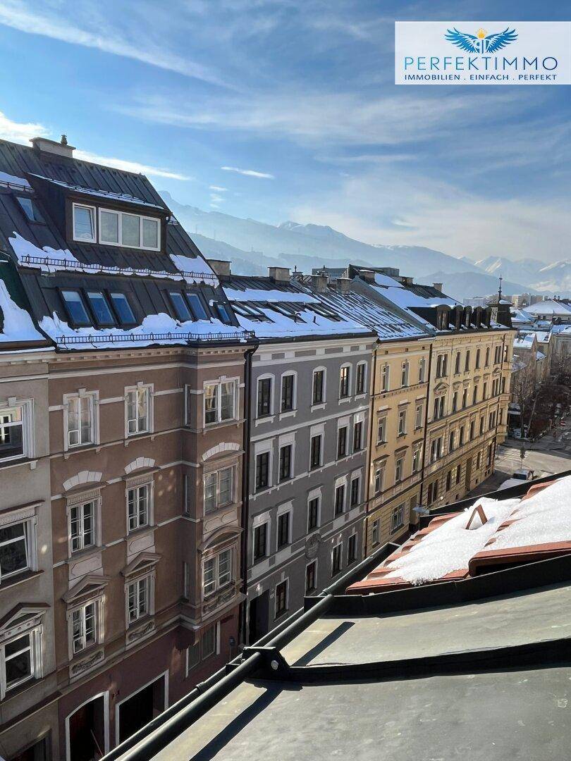 Dachlandschaft der Stadt mit historischen Gebäuden und schneebedeckten Bergen im Hintergrund.