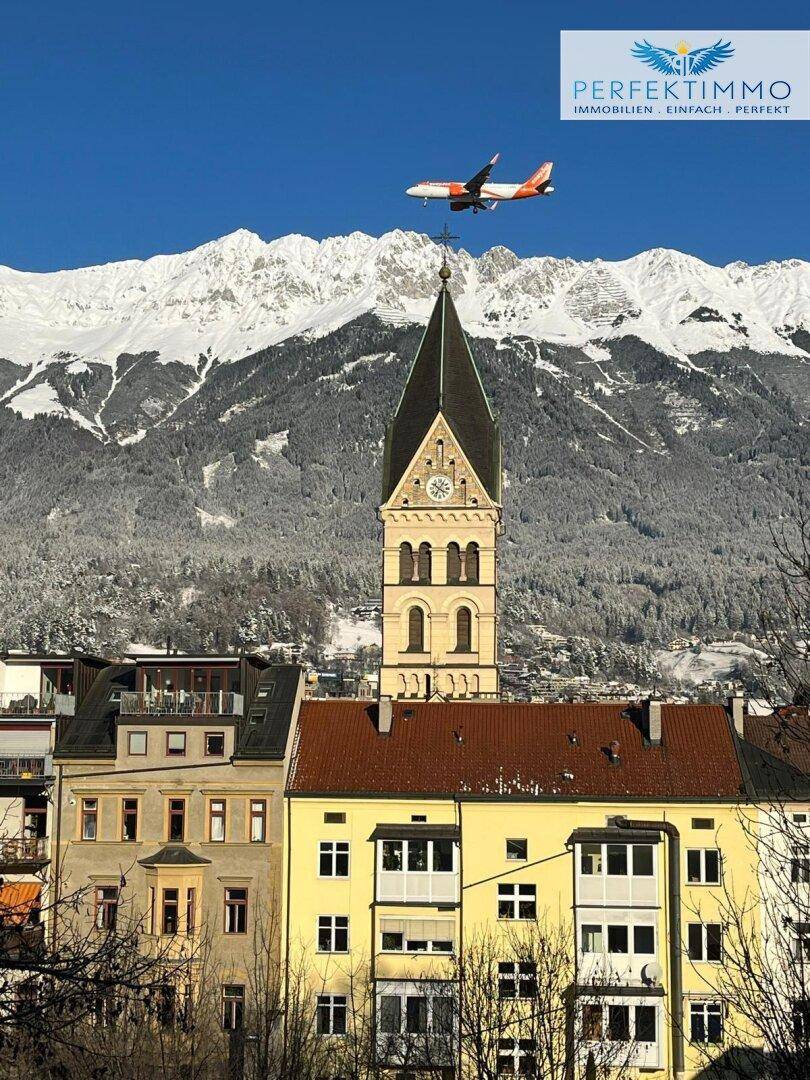 Winterlicher Panoramablick auf die Stadt mit Kirche, schneebedeckten Bergen und Flugzeug.