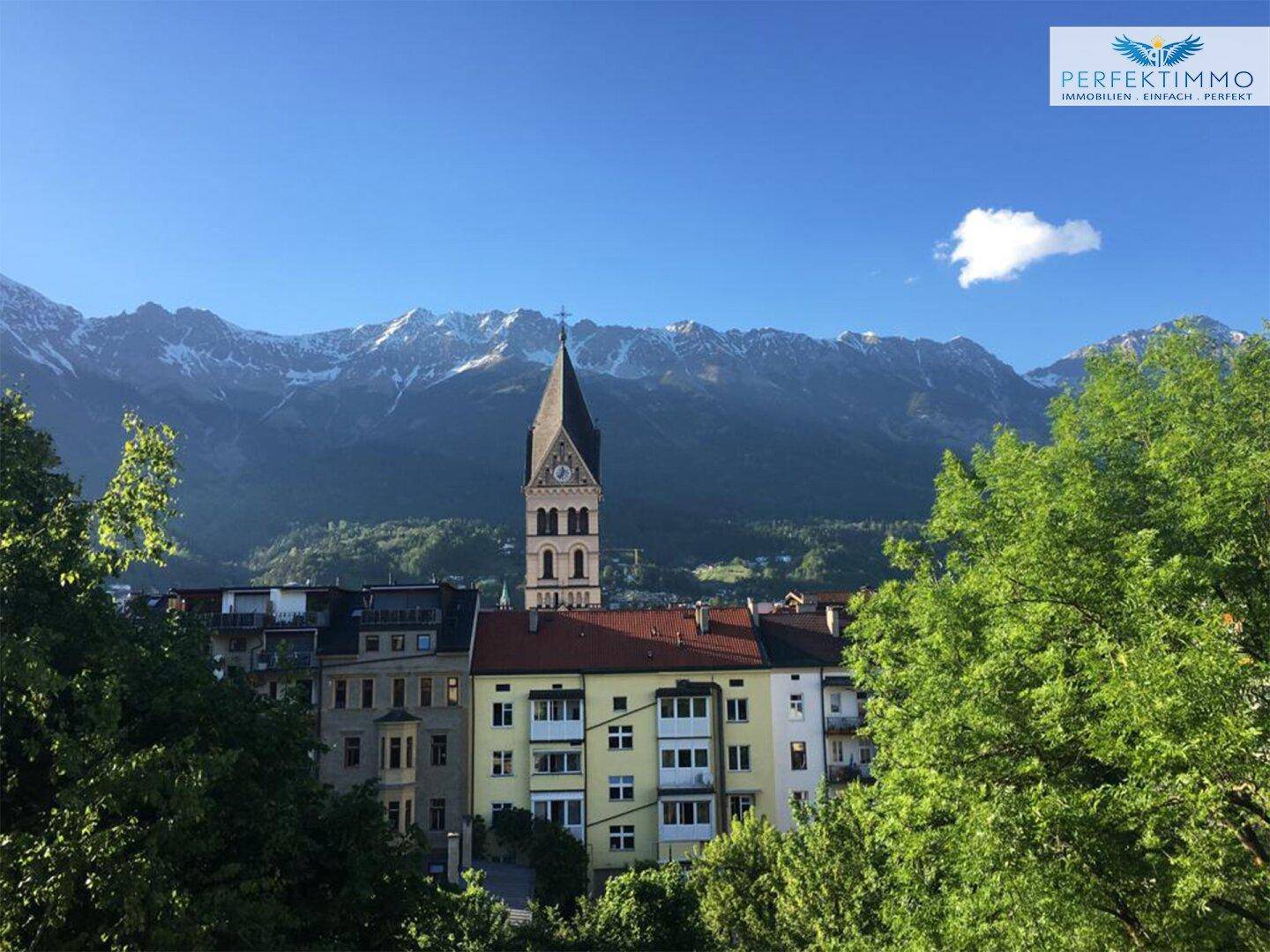 Panoramablick auf die Stadt mit Kirche und schneebedeckten Bergen im Hintergrund.