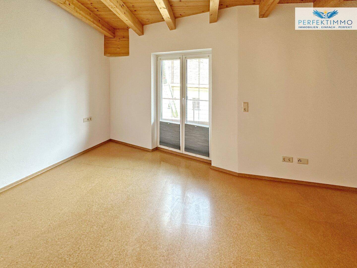 Gemütliches Zimmer mit Korkboden, Holzbalkendecke und Zugang zu einem Außenbereich.