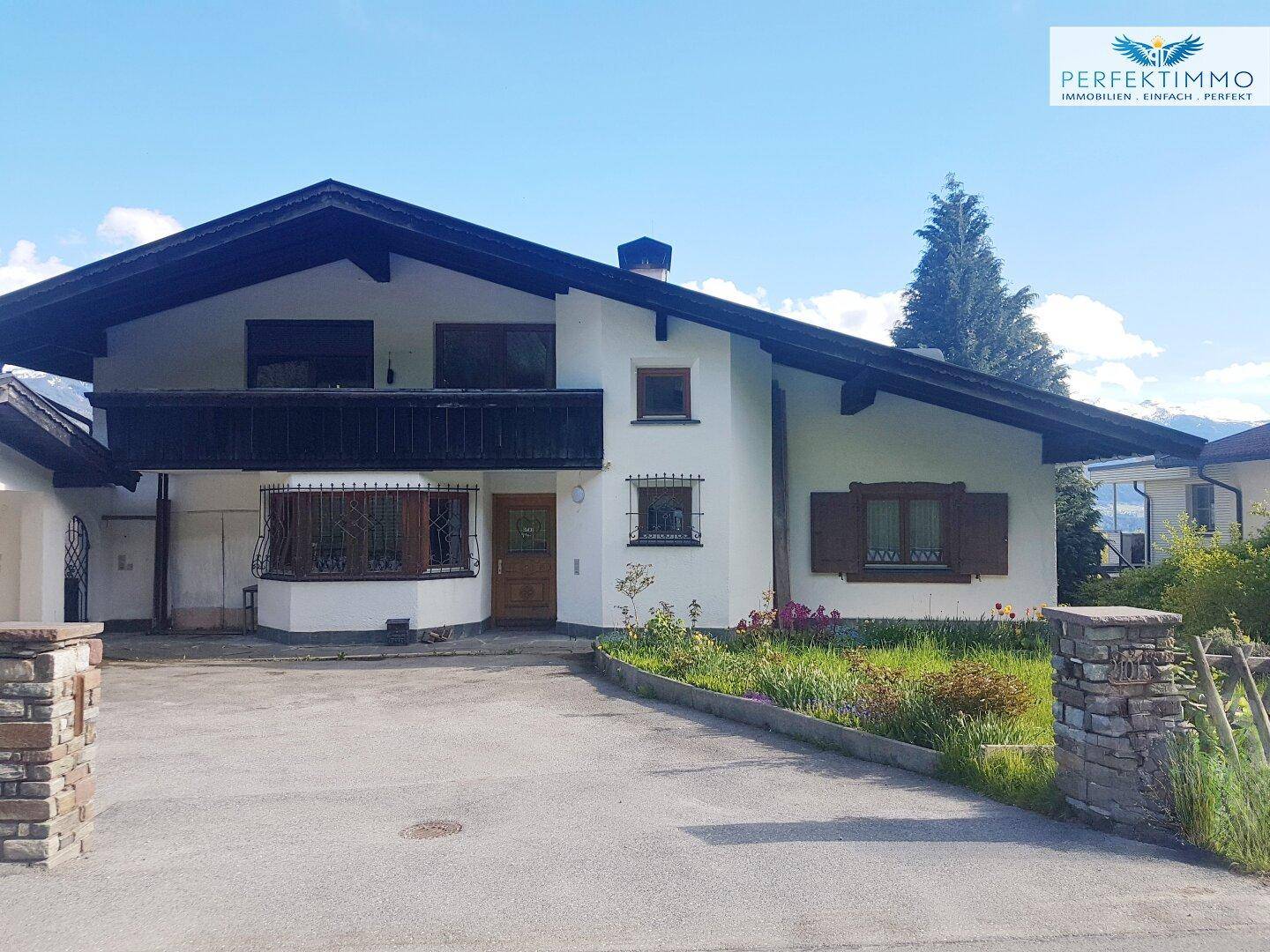 Traditionelles Einfamilienhaus mit Satteldach, Carport und gepflegtem Vorgarten unter blauem Himmel.