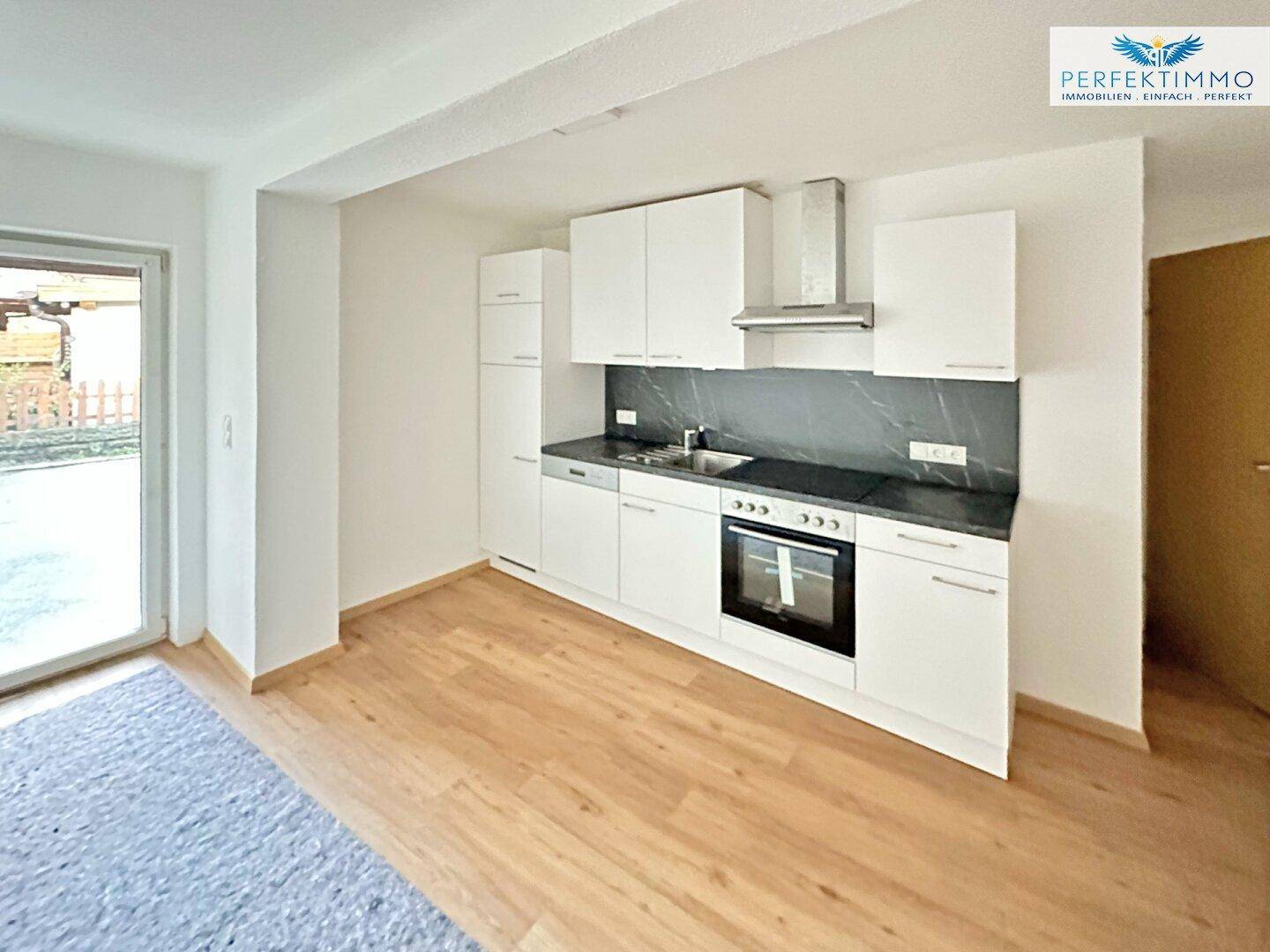 Moderne Einbauküche mit weißen Schränken, dunkler Arbeitsplatte und Holzboden.