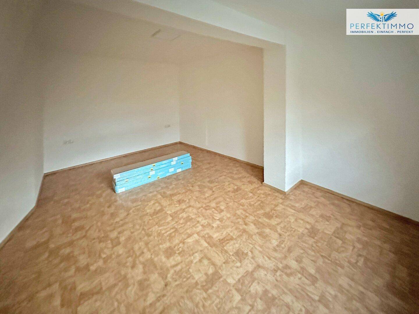 Leerer Raum mit Laminatboden, weißen Wänden und Baumaterialien.