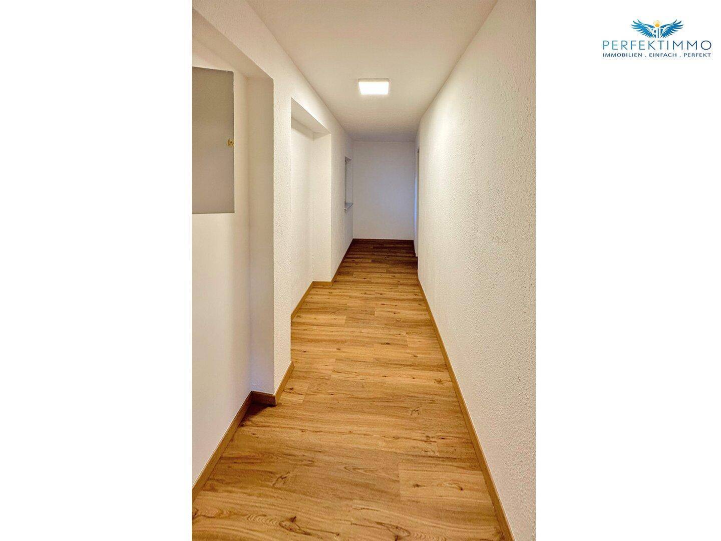 Heller Flur mit Laminatboden und weißen Wänden, der zu weiteren Räumen führt.