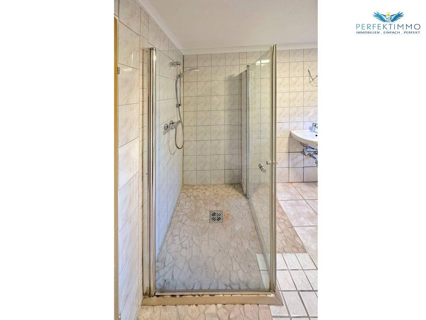 Duschbereich in einem gefliesten Badezimmer mit Glasabtrennung und Duschwanne.