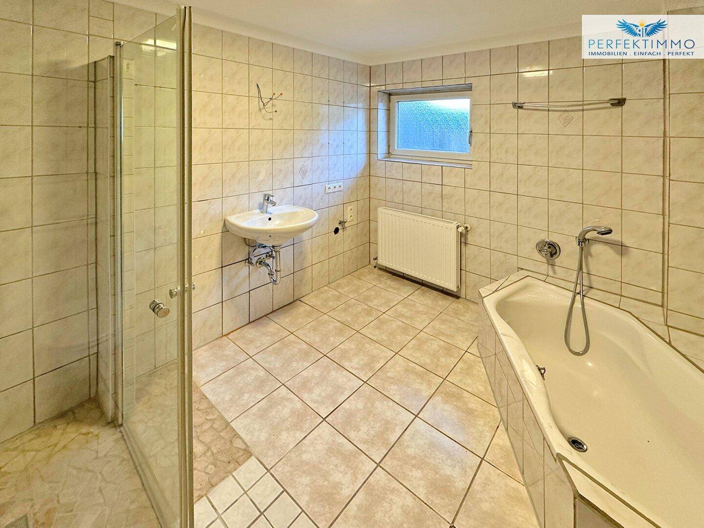 Gefliestes Badezimmer mit Badewanne, Dusche, Waschbecken und Fenster.
