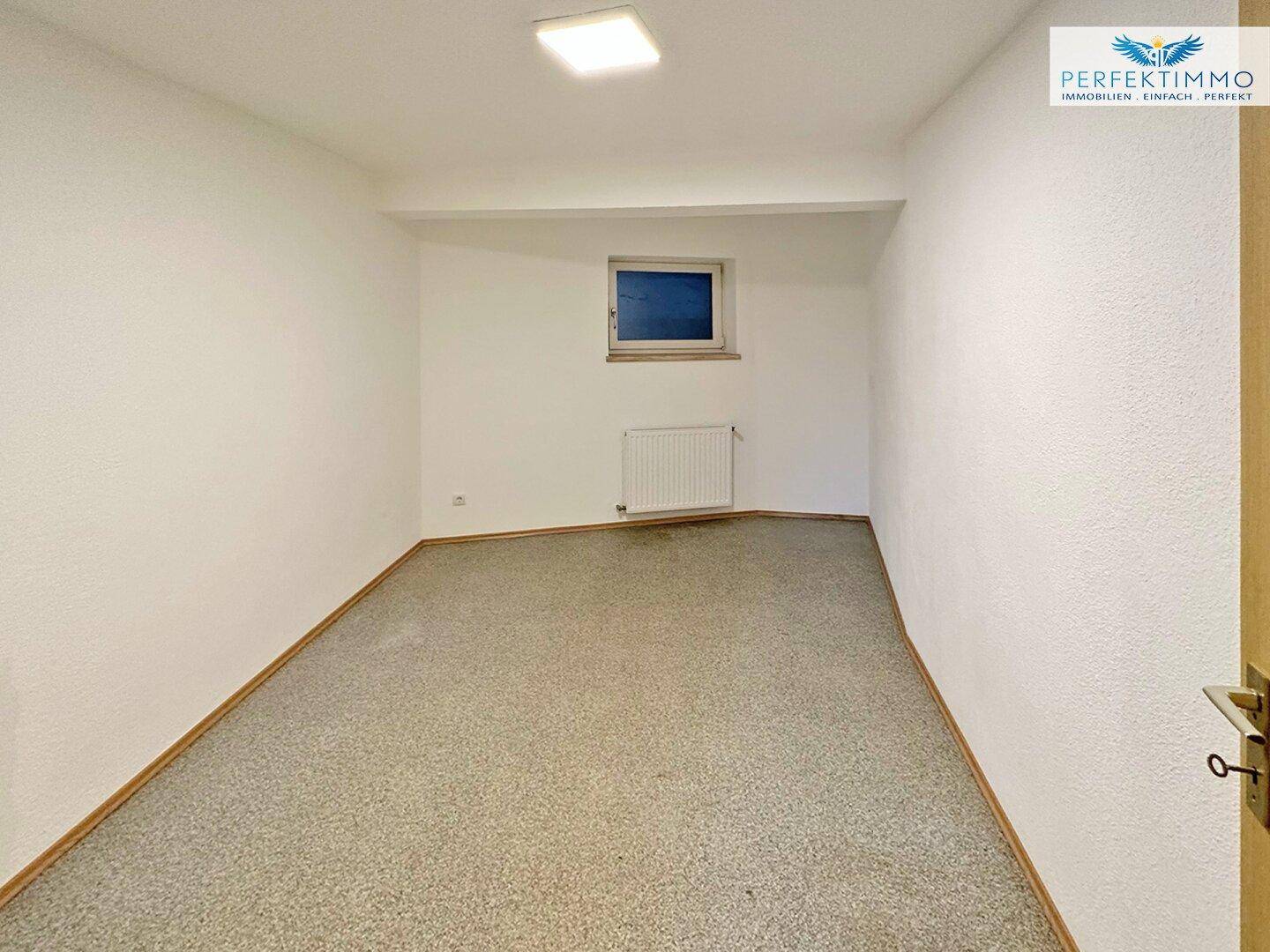 Kleiner Raum mit Teppichboden, weißen Wänden und einem Fenster.