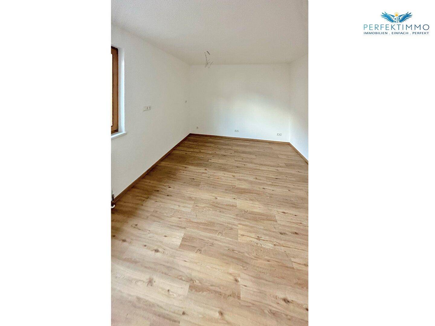 Leerer Raum mit Laminatboden und weißen Wänden, bereit zur individuellen Gestaltung.